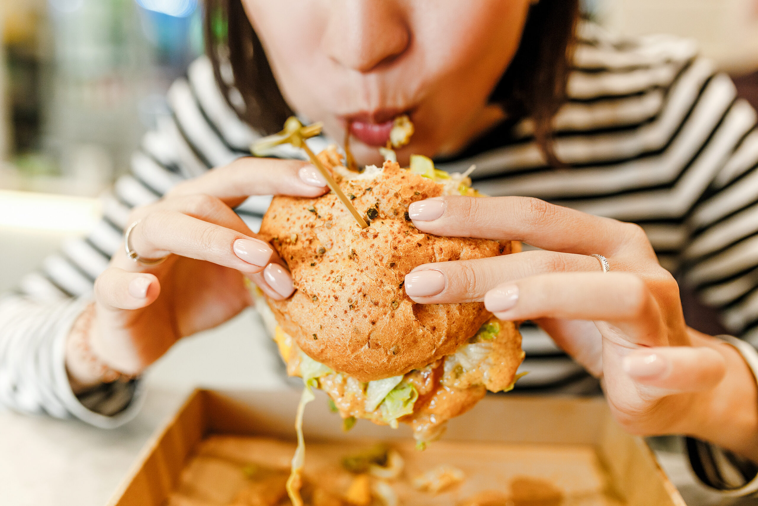 Asian woman eating a burger. He mouth is full and it looks like she just took a big bite.
