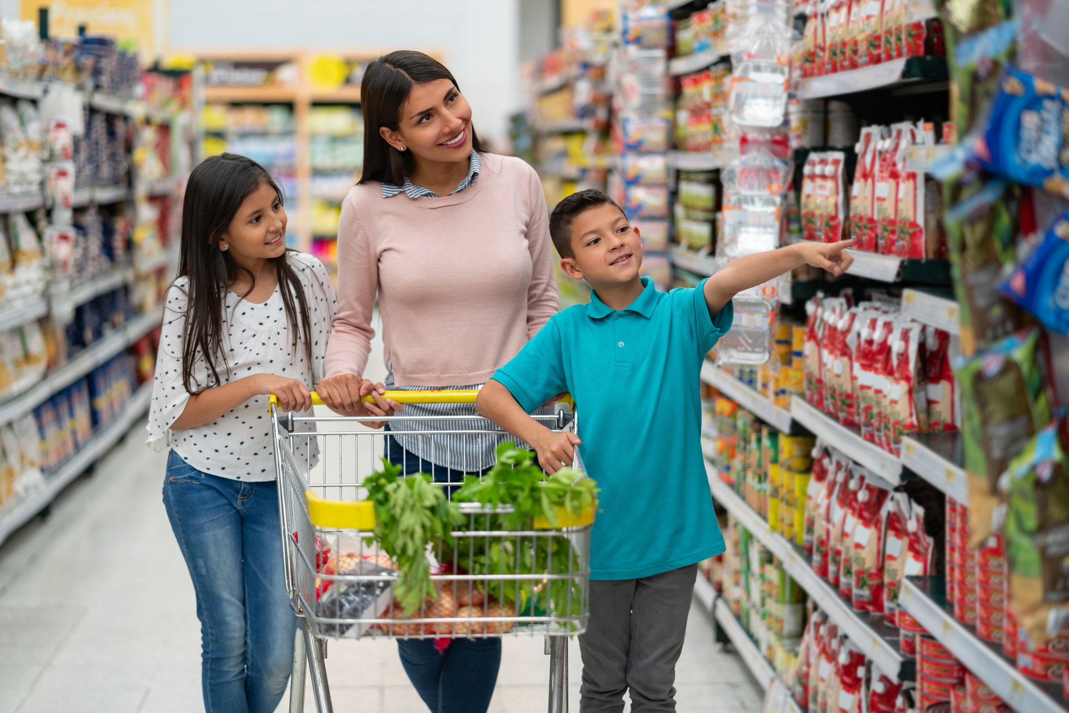 Beautiful latin american single parent with her two kids at the supermarket shopping for groceries and boy pointing at something