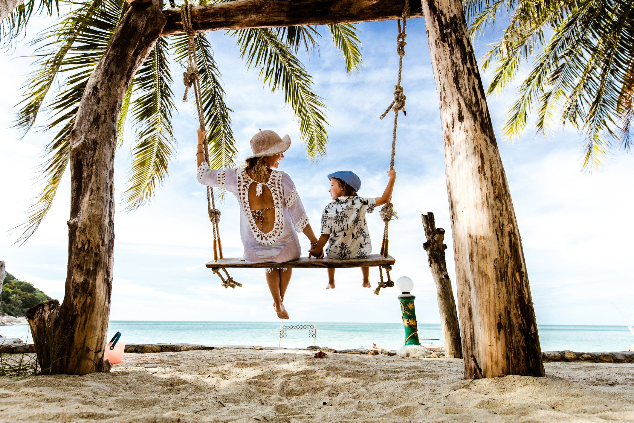 Rear view of carefree mother and son holding hands while swinging at the beach.