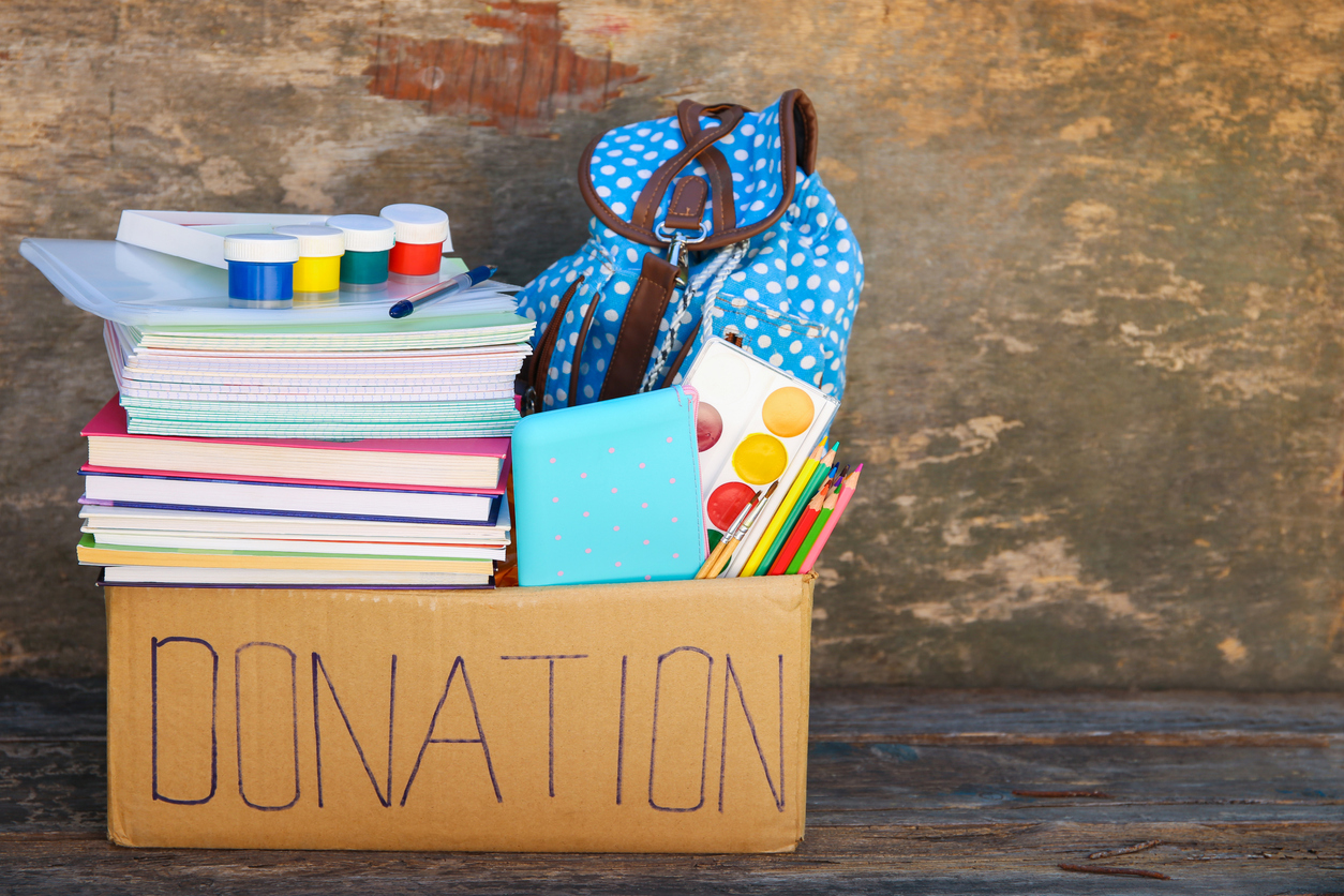 Donation box with school supplies on old wooden background.