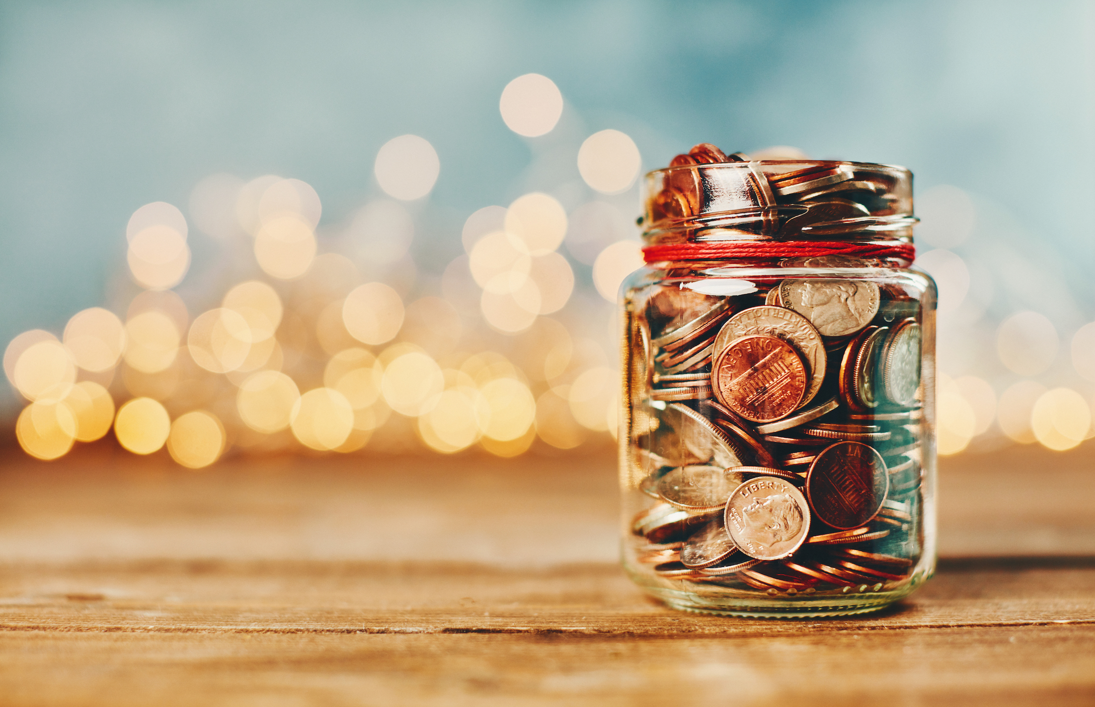 Donation money jar filled with coins in front of holiday lights money jar