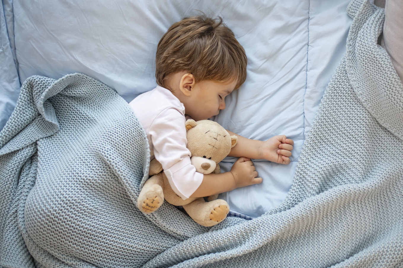 Photo of baby boy sleeping together with teddy bear.