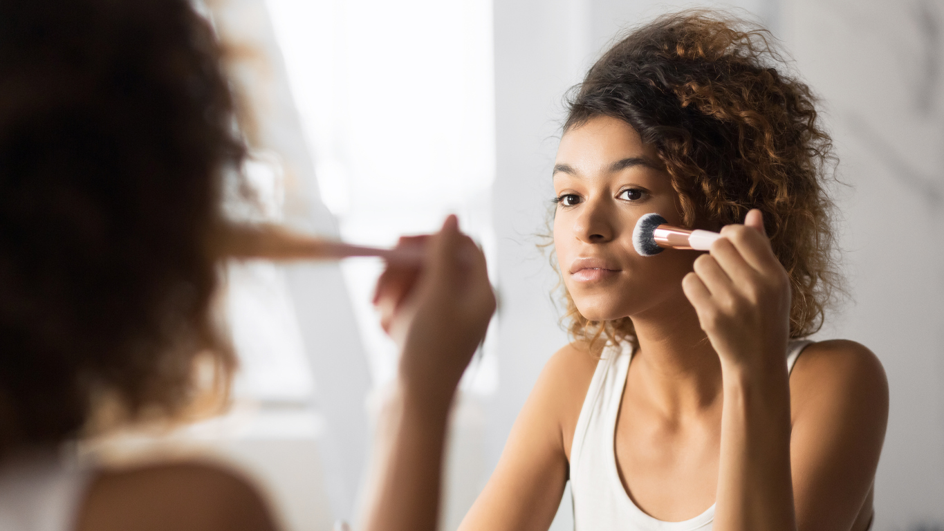 Afro Woman Applying Face Powder With Makeup Brush In Bathroom