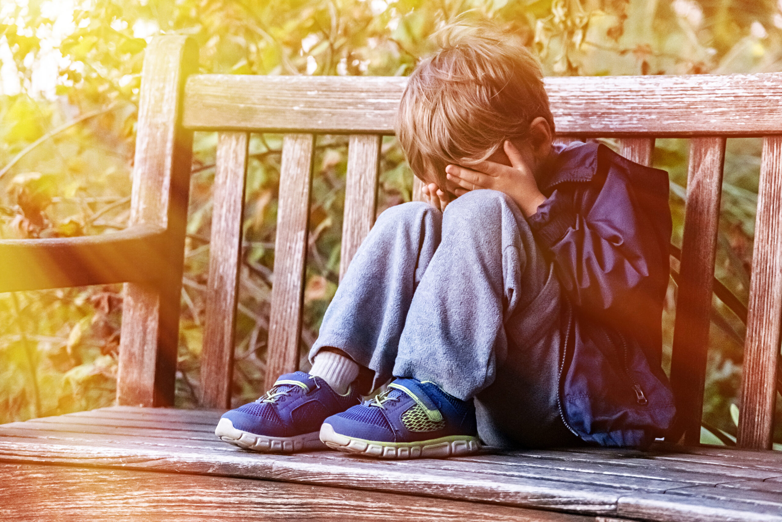 Crying child boy sitting on a bench covering his face