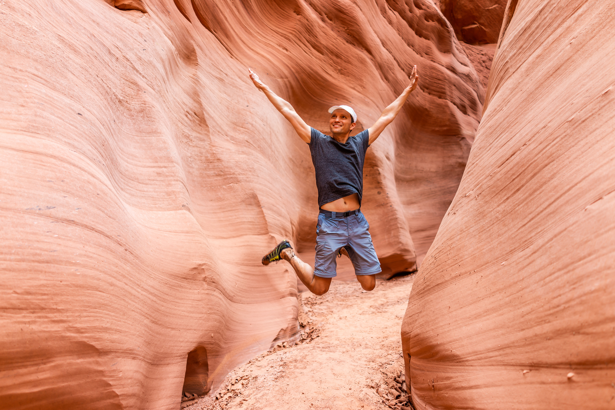 Man happy hiker jumping up arms raised by red wave shape formations at Antelope slot canyon in Arizona on footpath trail from Lake Powell