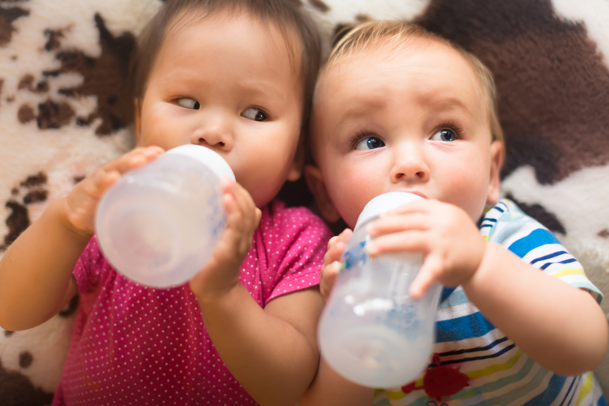 Mulitracial babies drinking bottles of milk together.