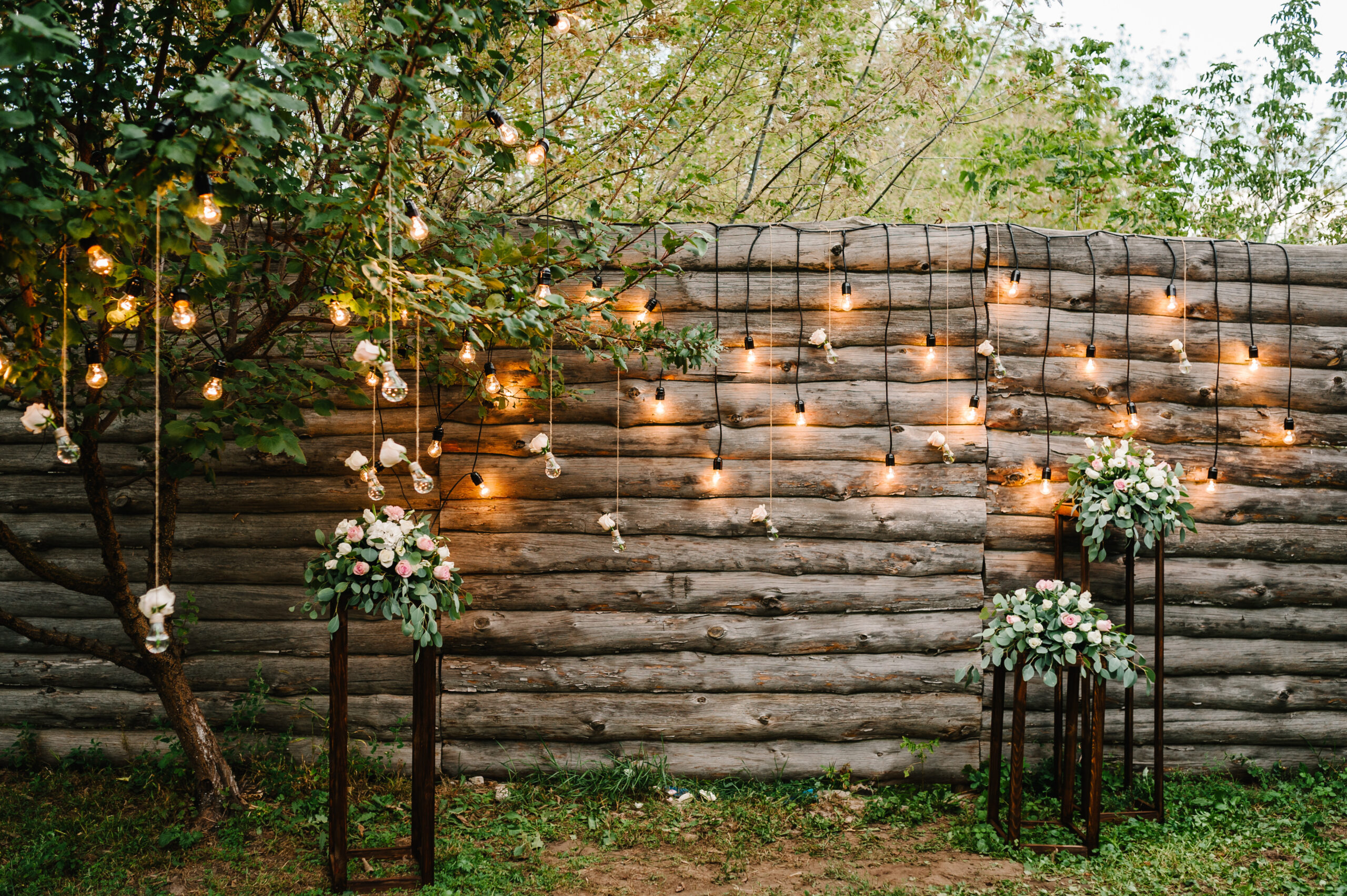 Wooden wall decorated garland with luminous bulbs and electric lamps decorated flowers. Original wedding floral decoration. Wedding. Reception. Lounge zone.