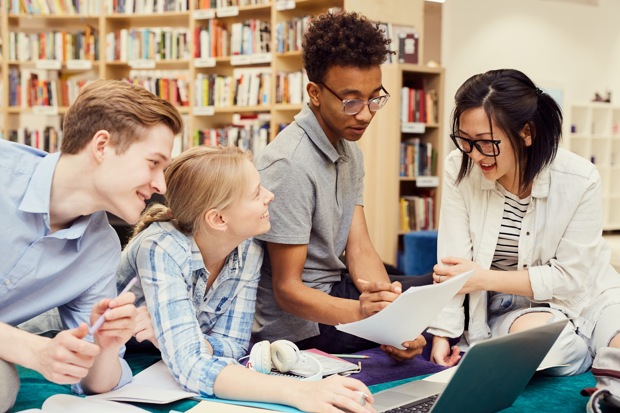 Group of positive young multi-ethnic students sitting in modern library and viewing curriculum while preparing for classes