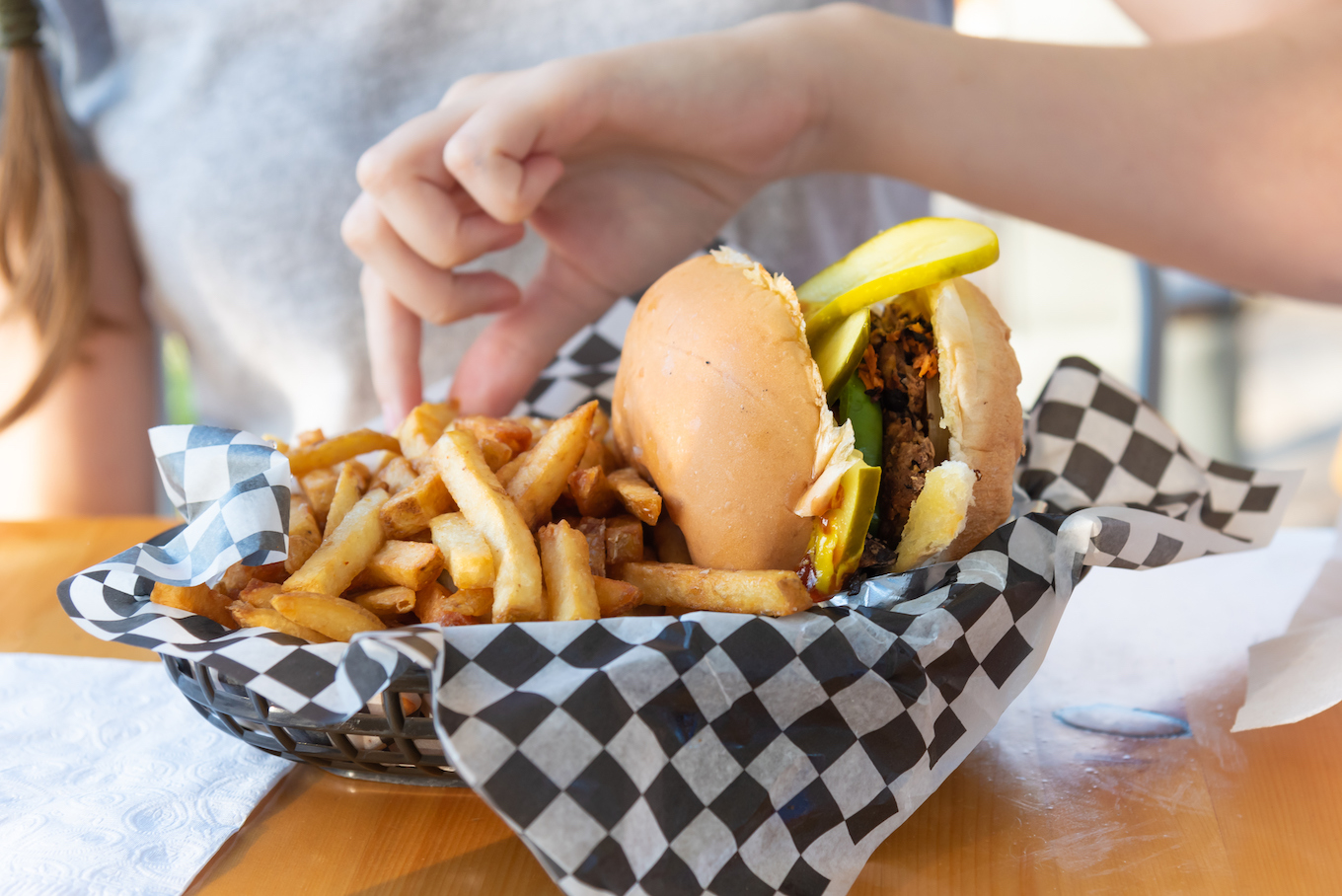 Vegan black-bean lentil hamburger and french fries in paper lined basket on restaurant patio table