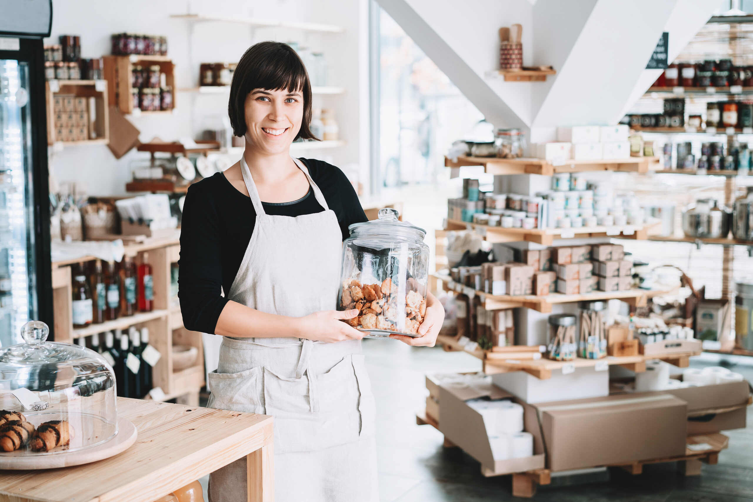 Small local business owner. Seller assistant with glass jar of pastries in interior of zero waste shop.