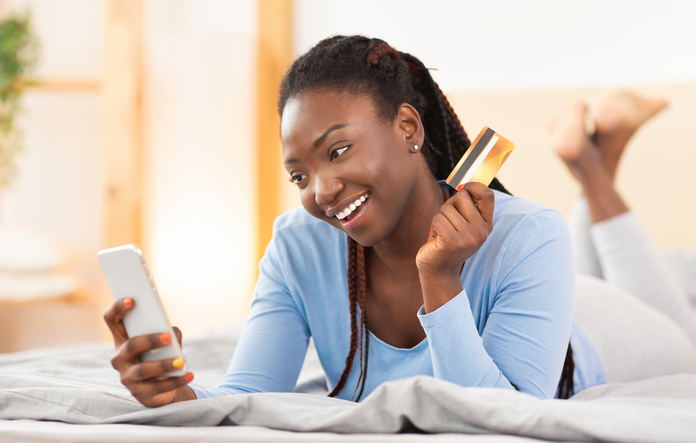 Happy Black Woman Using Phone Purchasing Online Lying In Bed