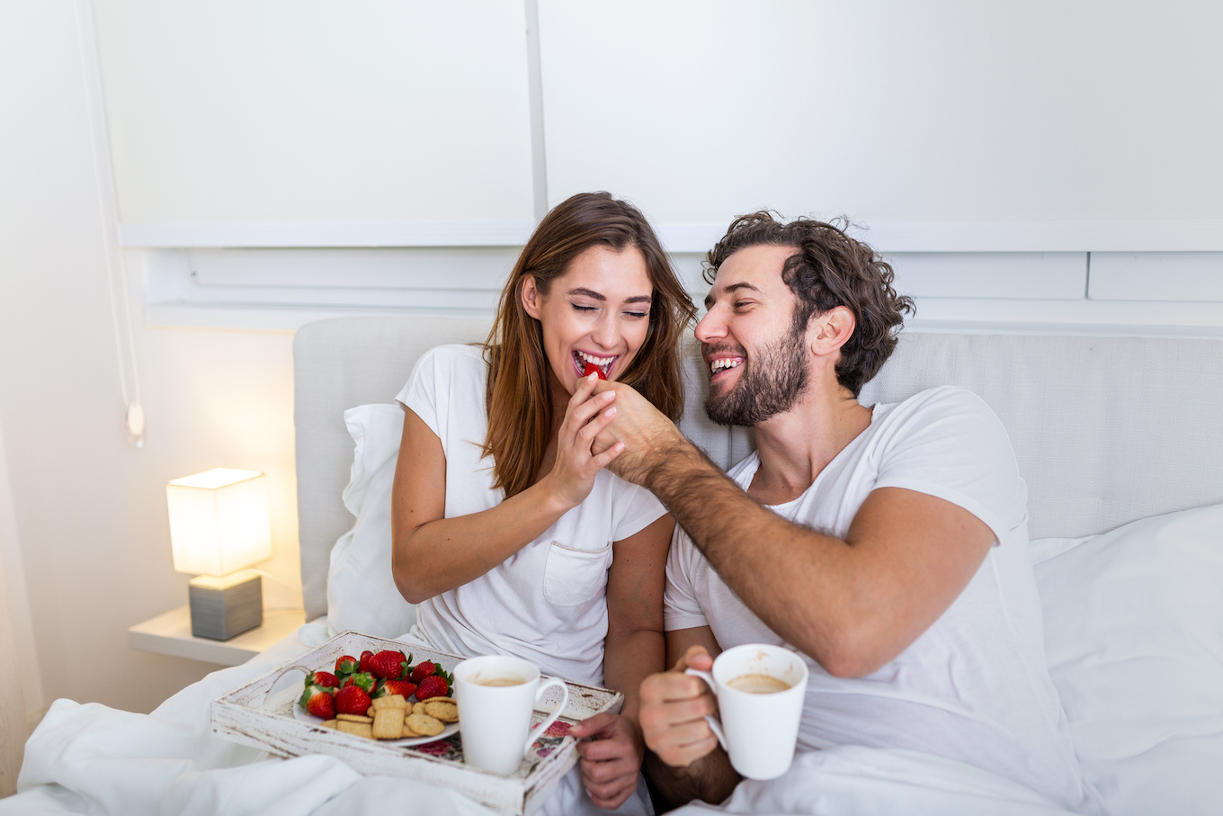 Couple in love having breakfast in bed. Young caucasian couple having romantic breakfast in bed. Female and male , two cups of coffee, fruits and colorful biscuits.