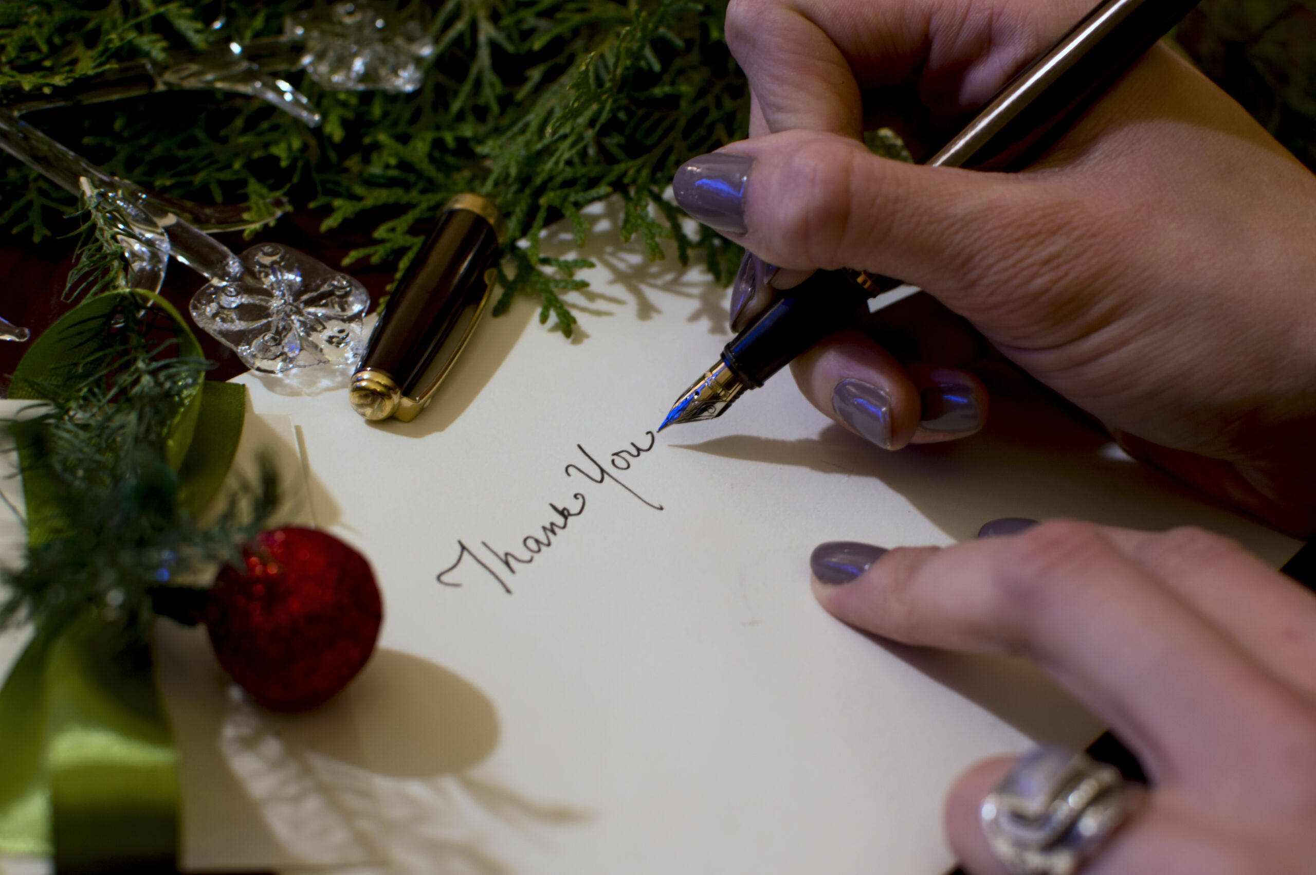 Woman writing Christmas card writing thank you with evergreen and ornaments background