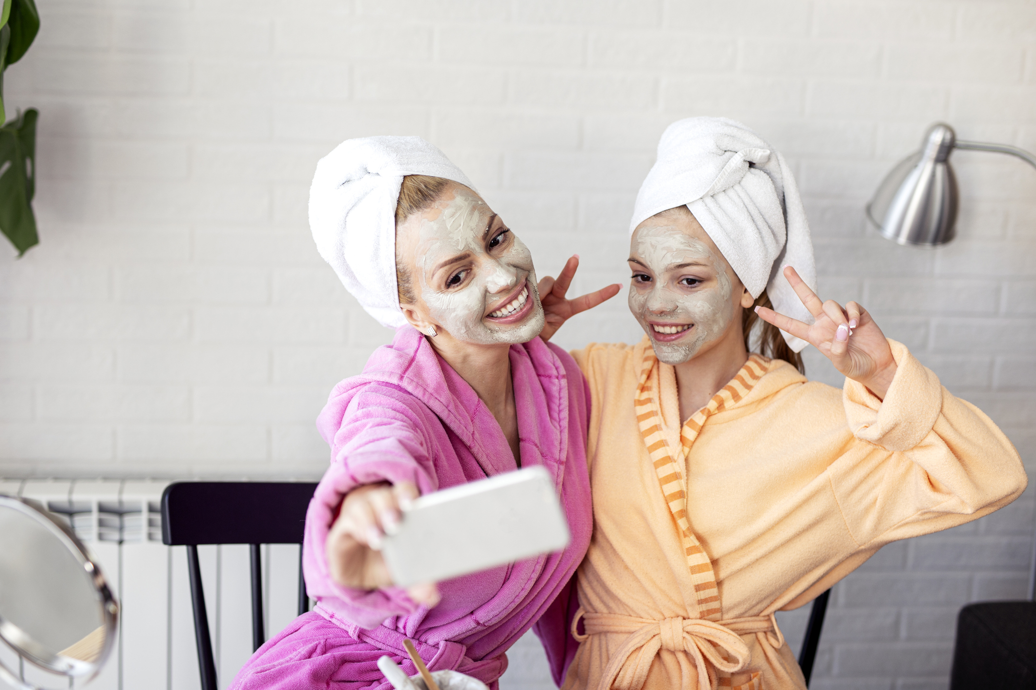 Mother and her daughter taking selfie by phone with facial mask and towel on head