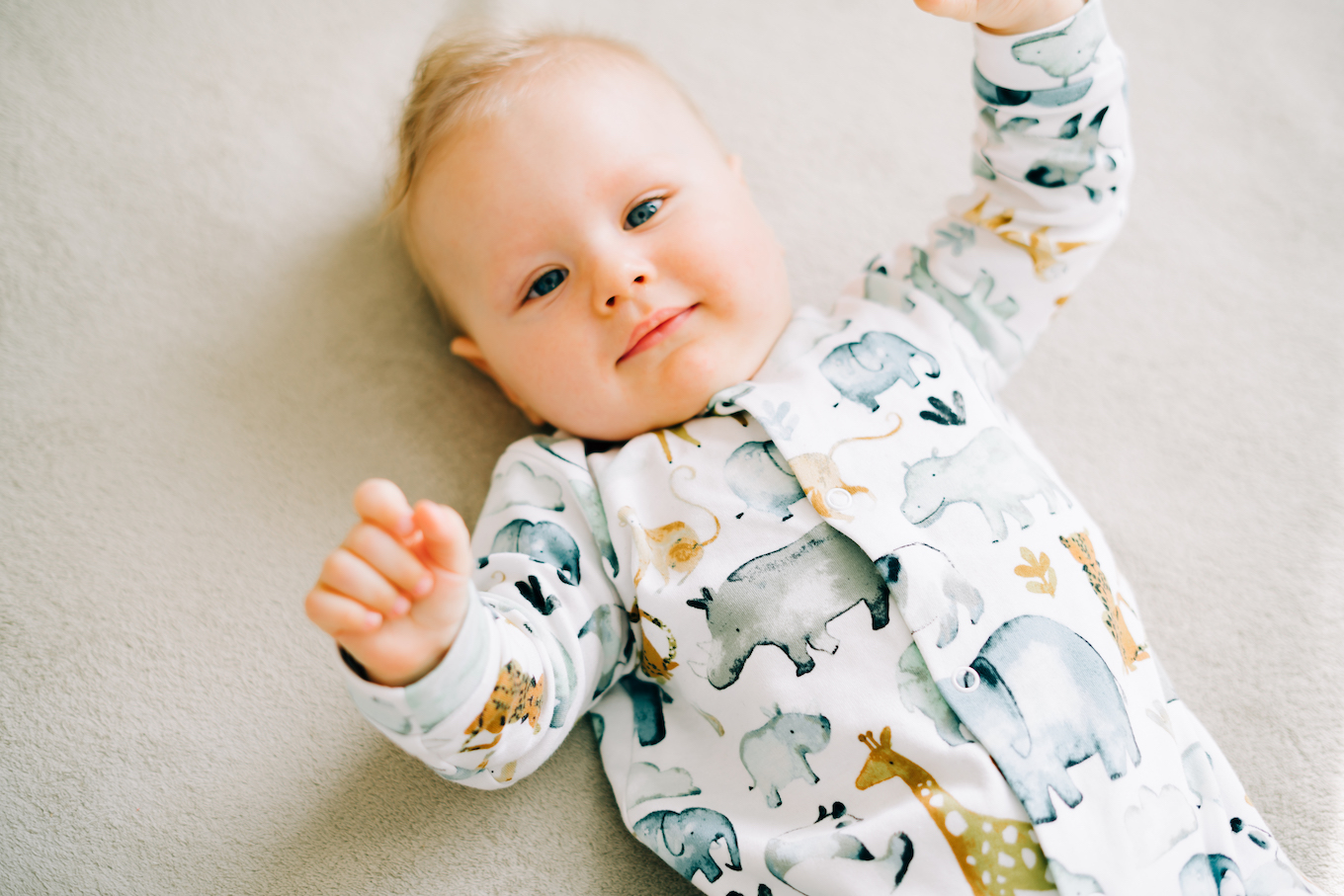 a small beautiful boy in a jumpsuit with animals is lying on the couch and looking at the camera