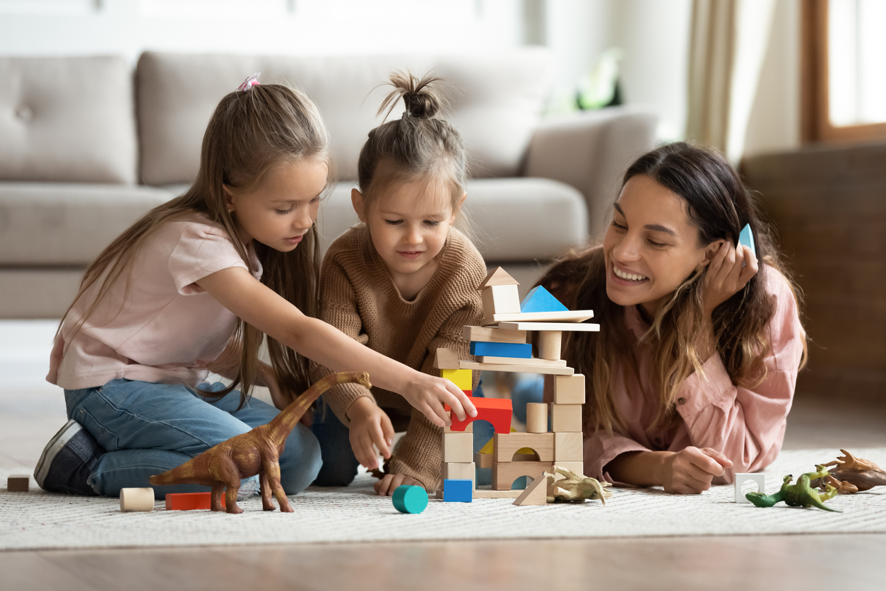 Young mom playing with building bricks with little daughters