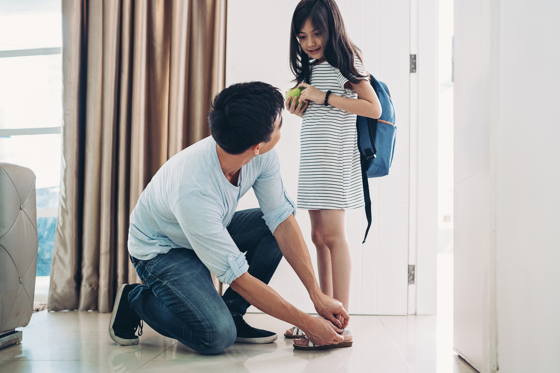 Father fastening his daughter's shoes at the doorway