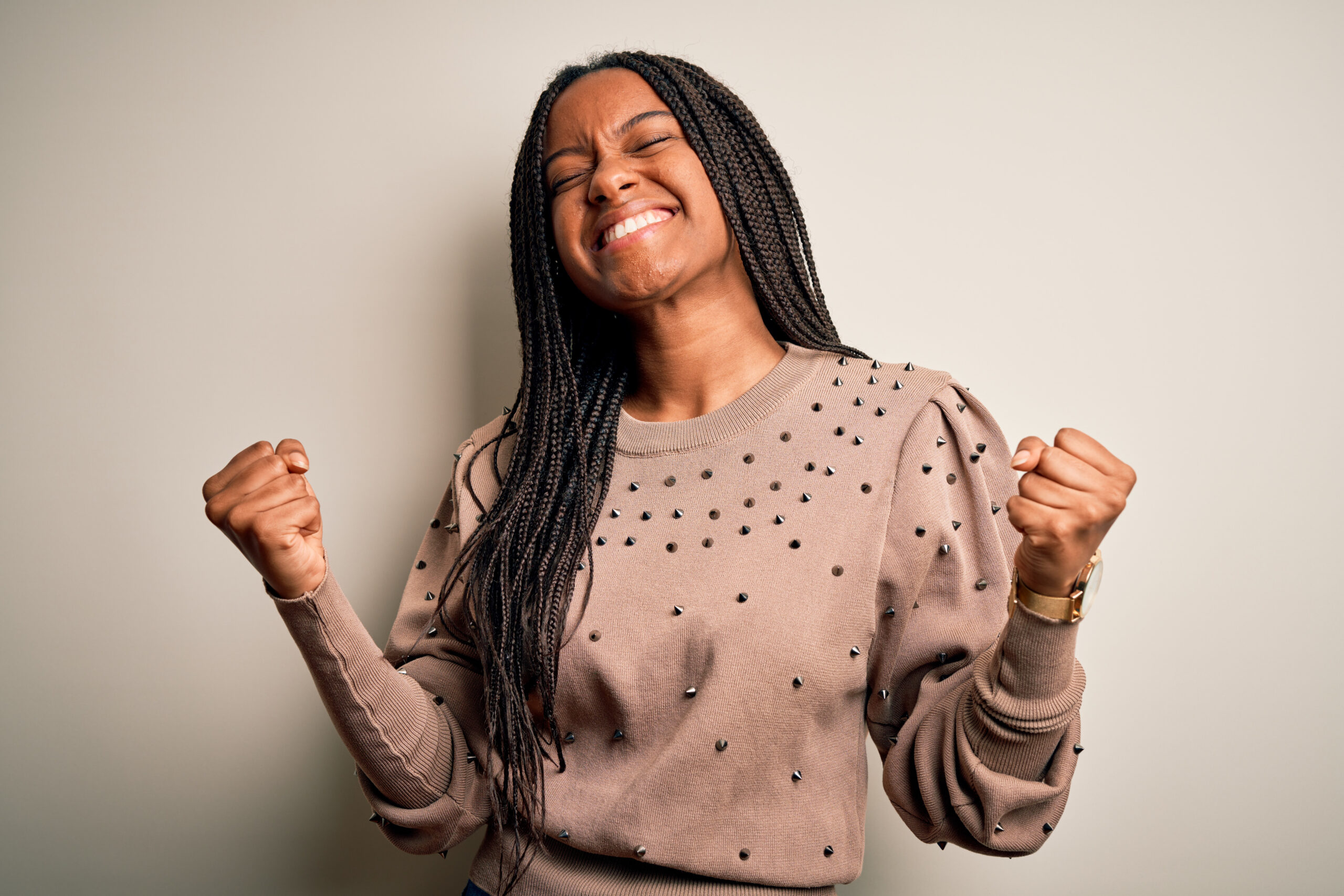 Young african american fashion woman standing casual over brown isolated background very happy and excited doing winner gesture with arms raised, smiling and screaming for success. Celebration concept.