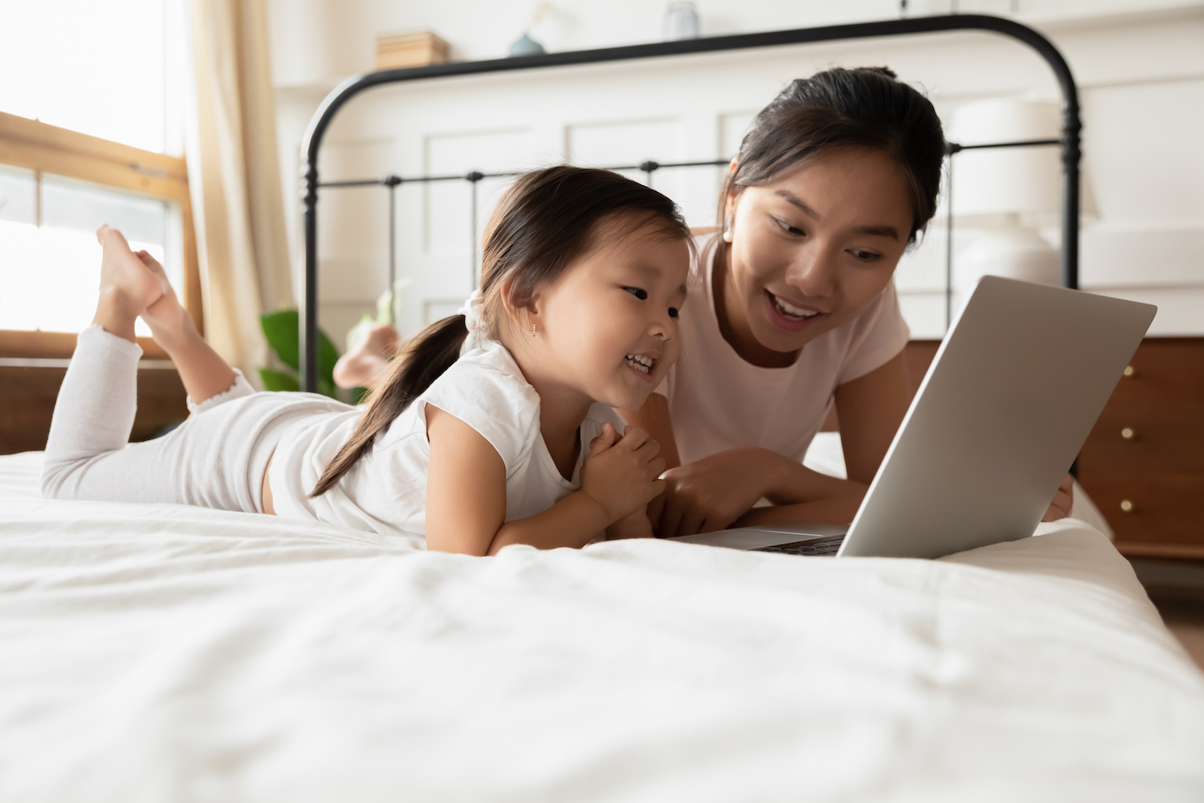 Asian mother and little daughter lying in bed with laptop Asian mother and little daughter lying in bed with laptop