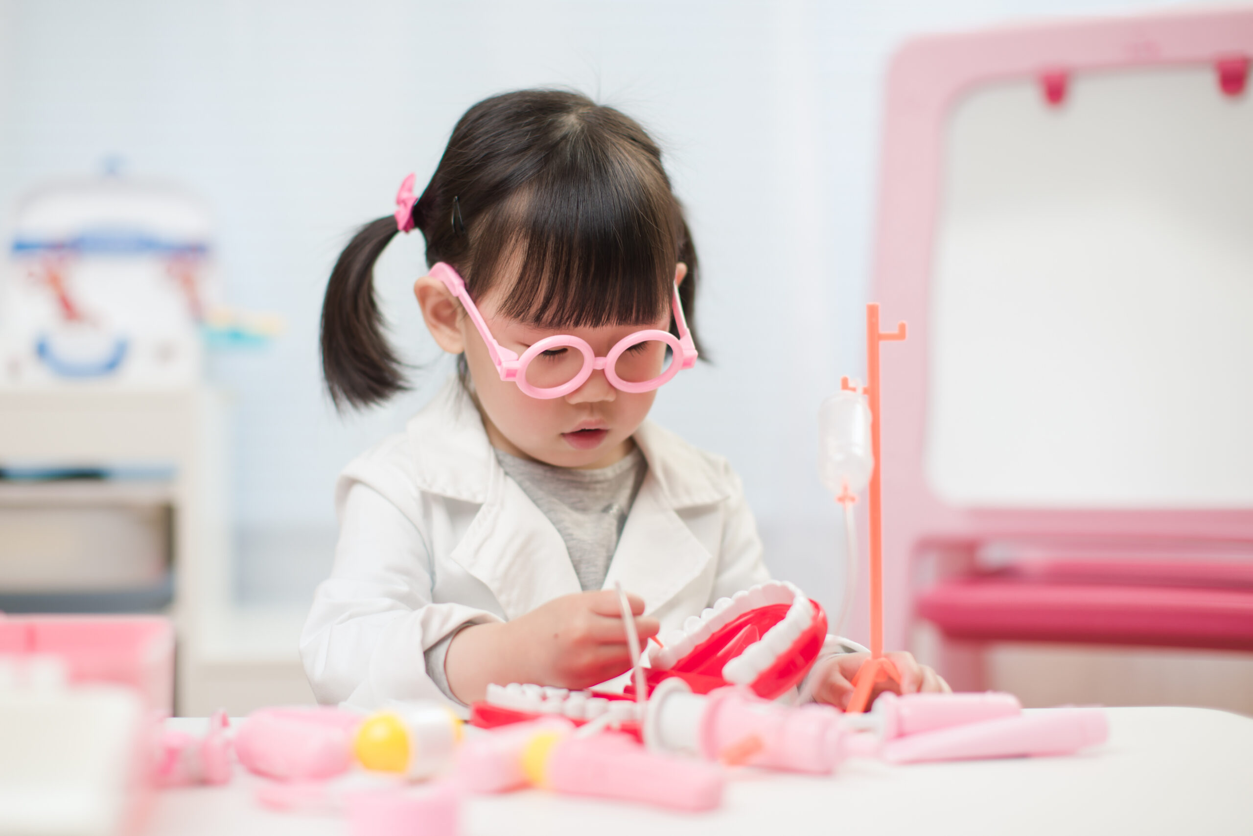 toddler girl pretend play dentist role at home against white background