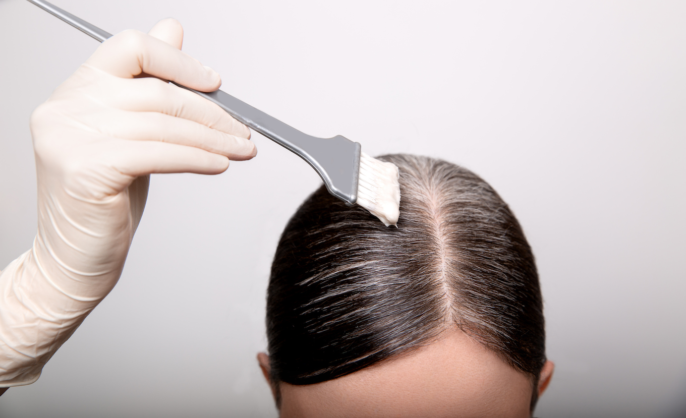 Woman dyeing gray hair root with brush and hair color, close up