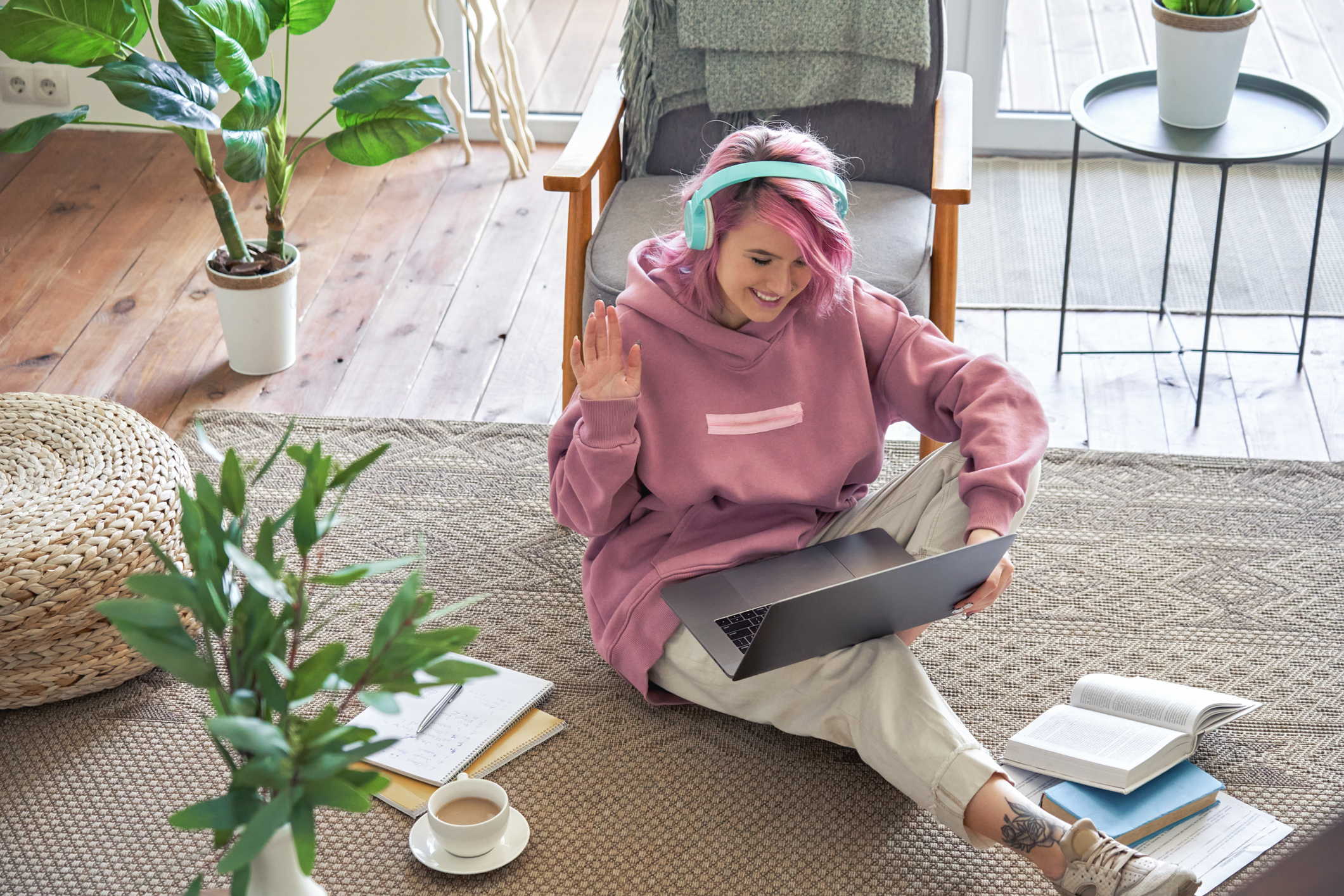 Happy teen girl school college student pink hair wear headphone waving hand video conference calling on laptop computer sit on floor distance learn zoom online virtual meeting at home office. Top view