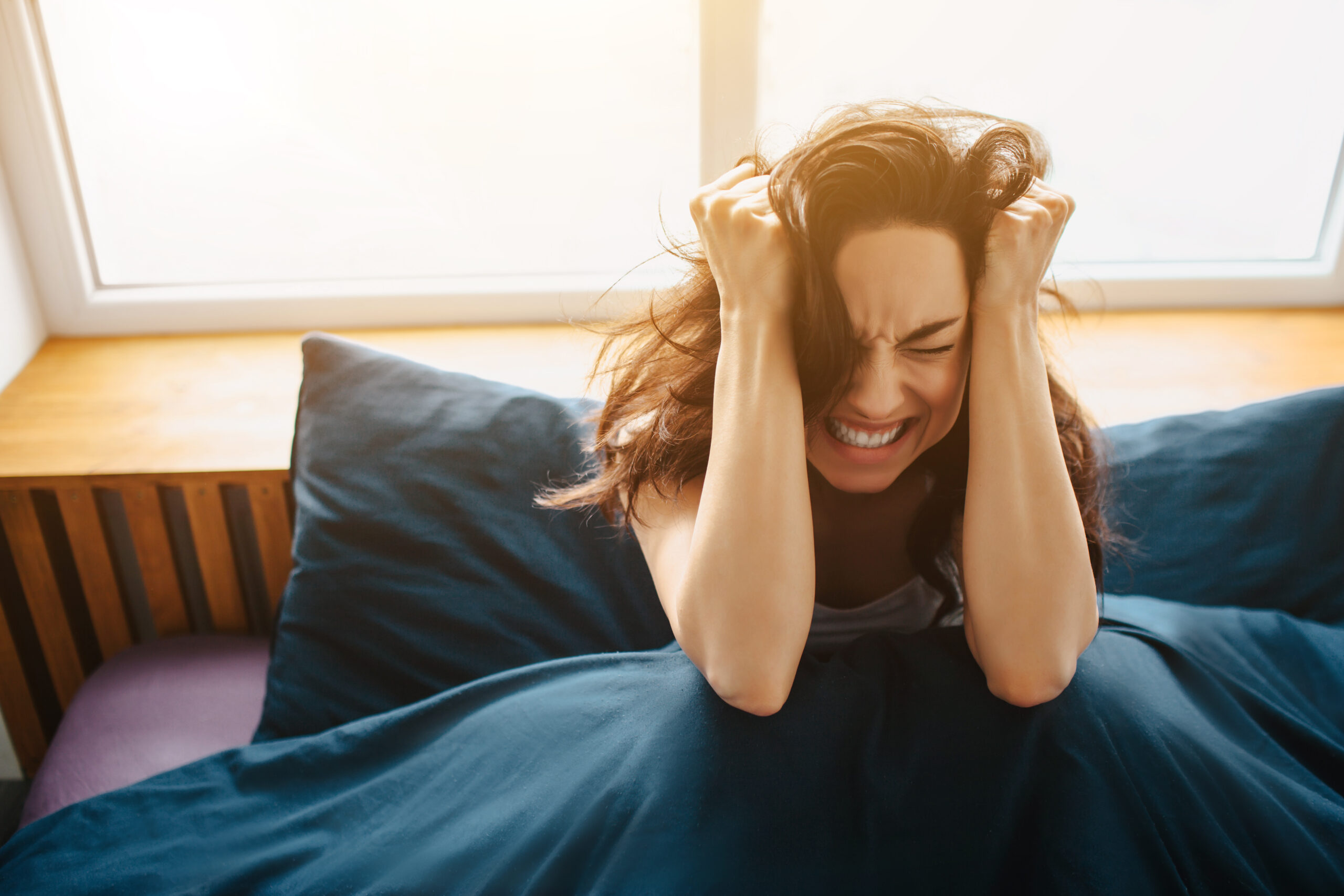 Young beautiful woman in morning bed at home. Hold hands on head close to ears and suffer from pain and headache. Strees and painful morning.