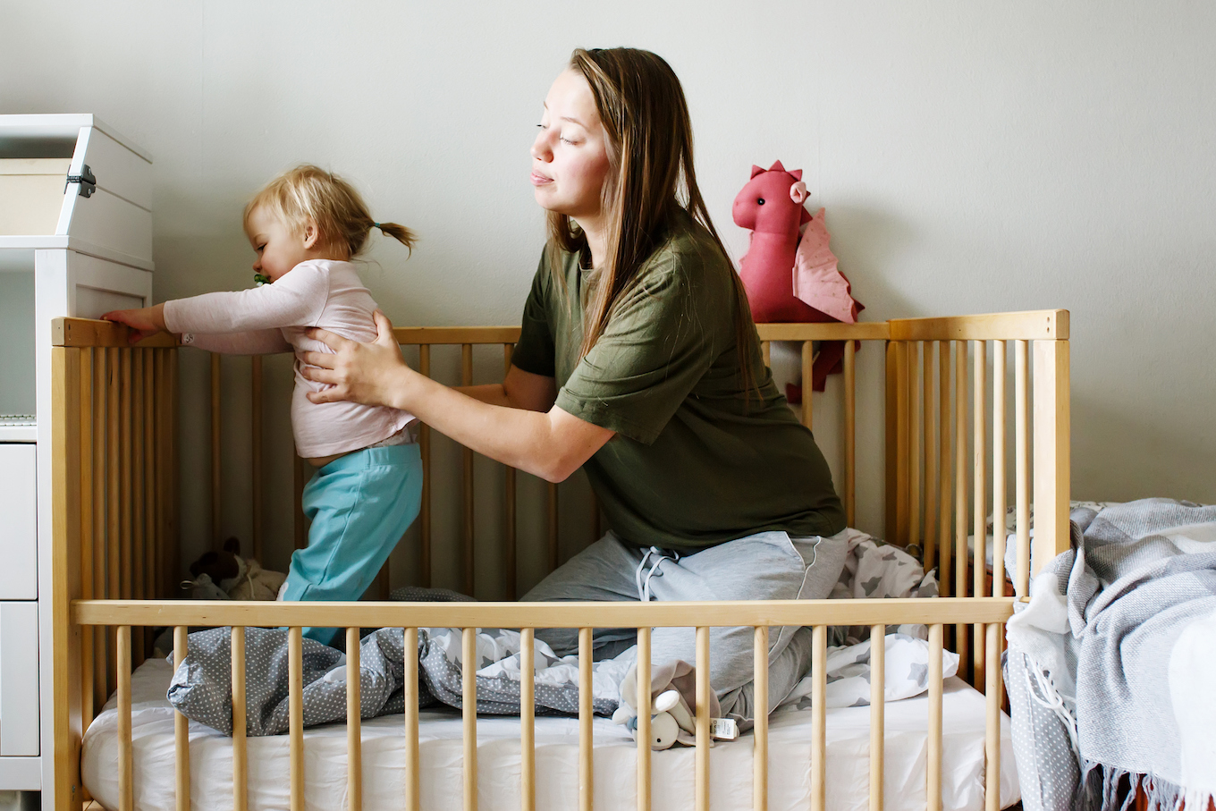 Young beautiful mother holding her toddler baby girl sitting together in a cot