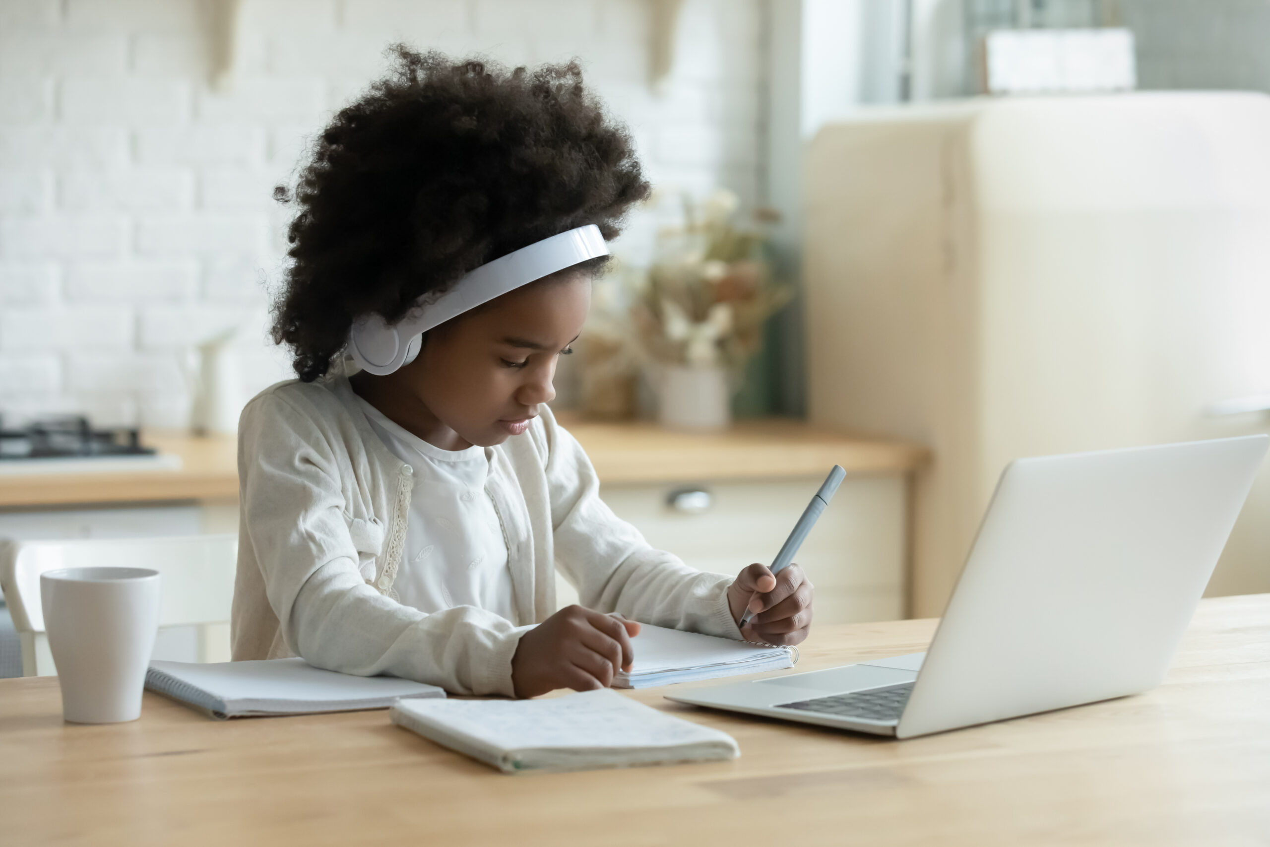 African schoolgirl in headphones using laptop do homework at home