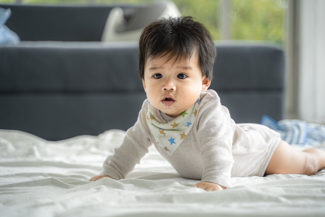 An Asian baby is crawling along the floor on a room covered by a quilt.