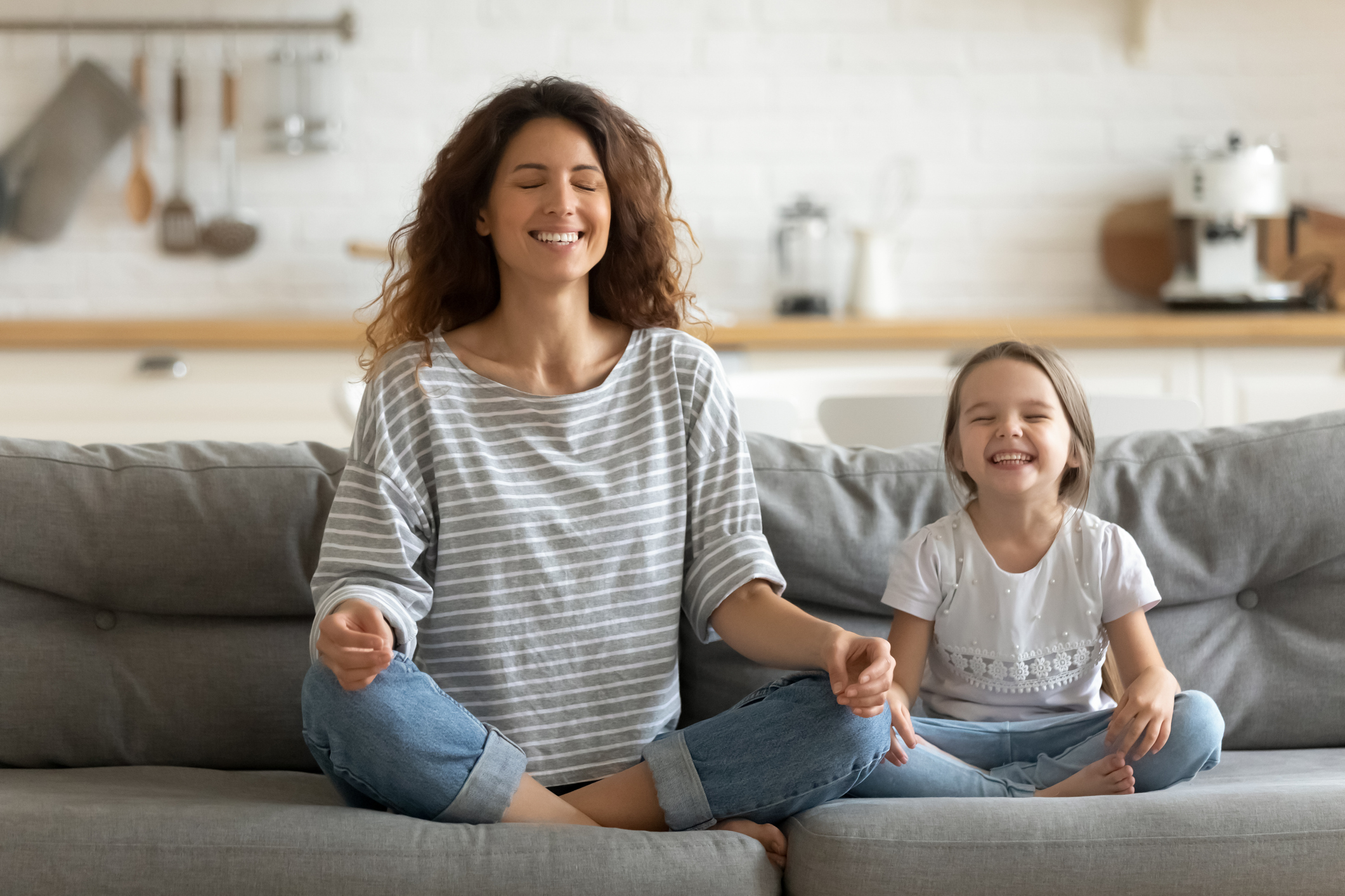 Happy young nanny mom teaching small daughter yoga breathing exercise.