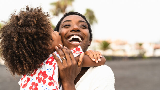mom and daughter hugging. daughter is kissing cheek of mom who is smiling