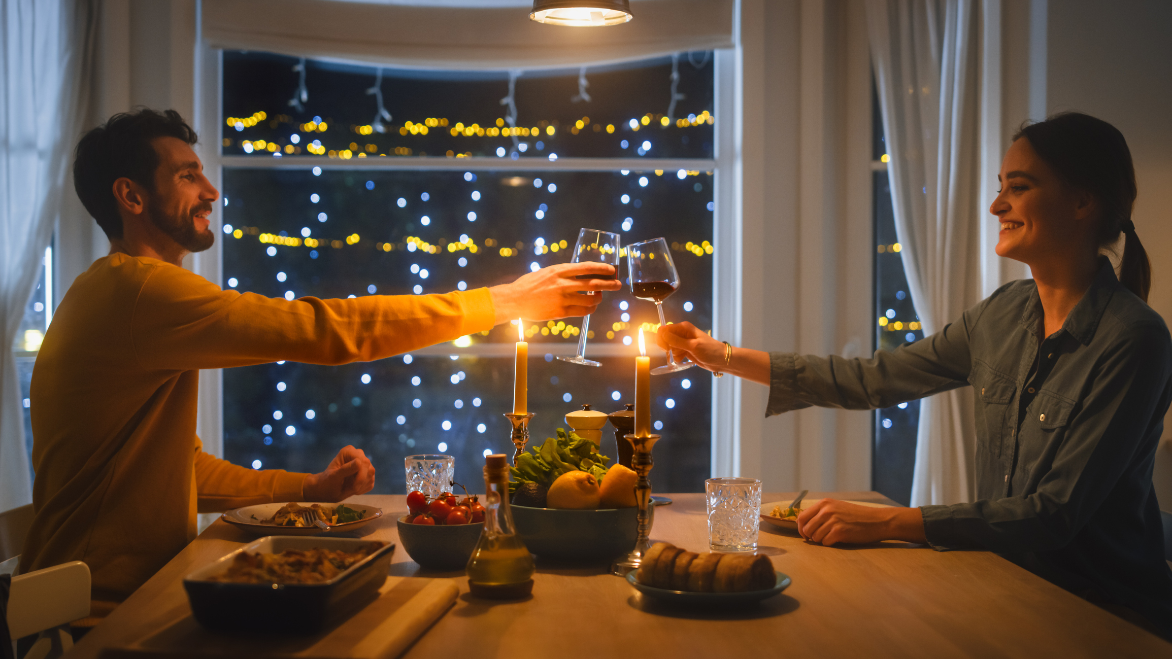 Happy Young Couple in Love Have Romantic Dinner, Toasting Each other with Glasses of Wine, Eating Tasty Meal in the Kitchen, Celebrating, Talking. Beautiful Lovely Husband and Wife Have Romantic Time