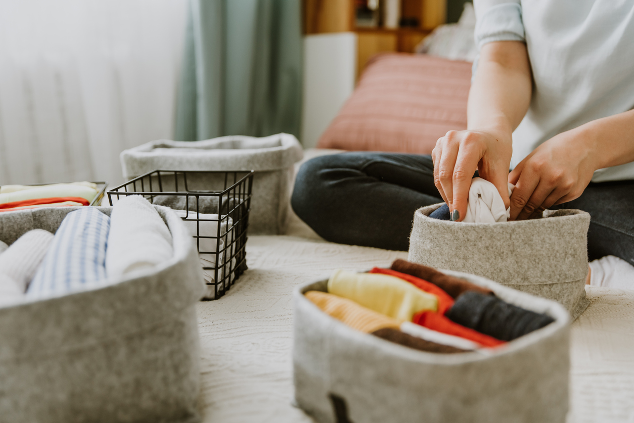 Woman organizing clothes in wardrobe, putting shirts in boxes, baskets into shelves. Clothes neatly folded after laundry. Concept of minimalist lifestyle