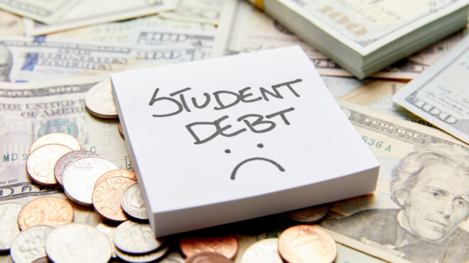 Student Loan Debt with sad face written on white sticky note on top of cash money with stack of money and coins
