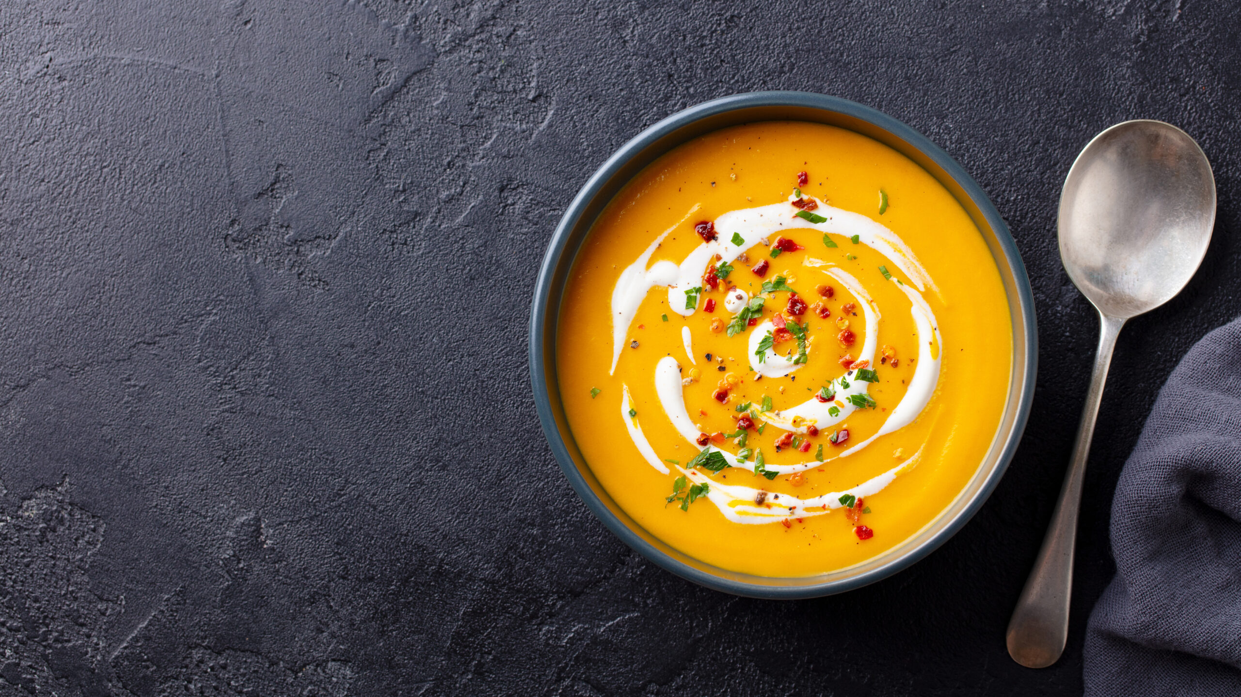 Pumpkin and carrot soup with cream in black bowl. Dark background. Top view.