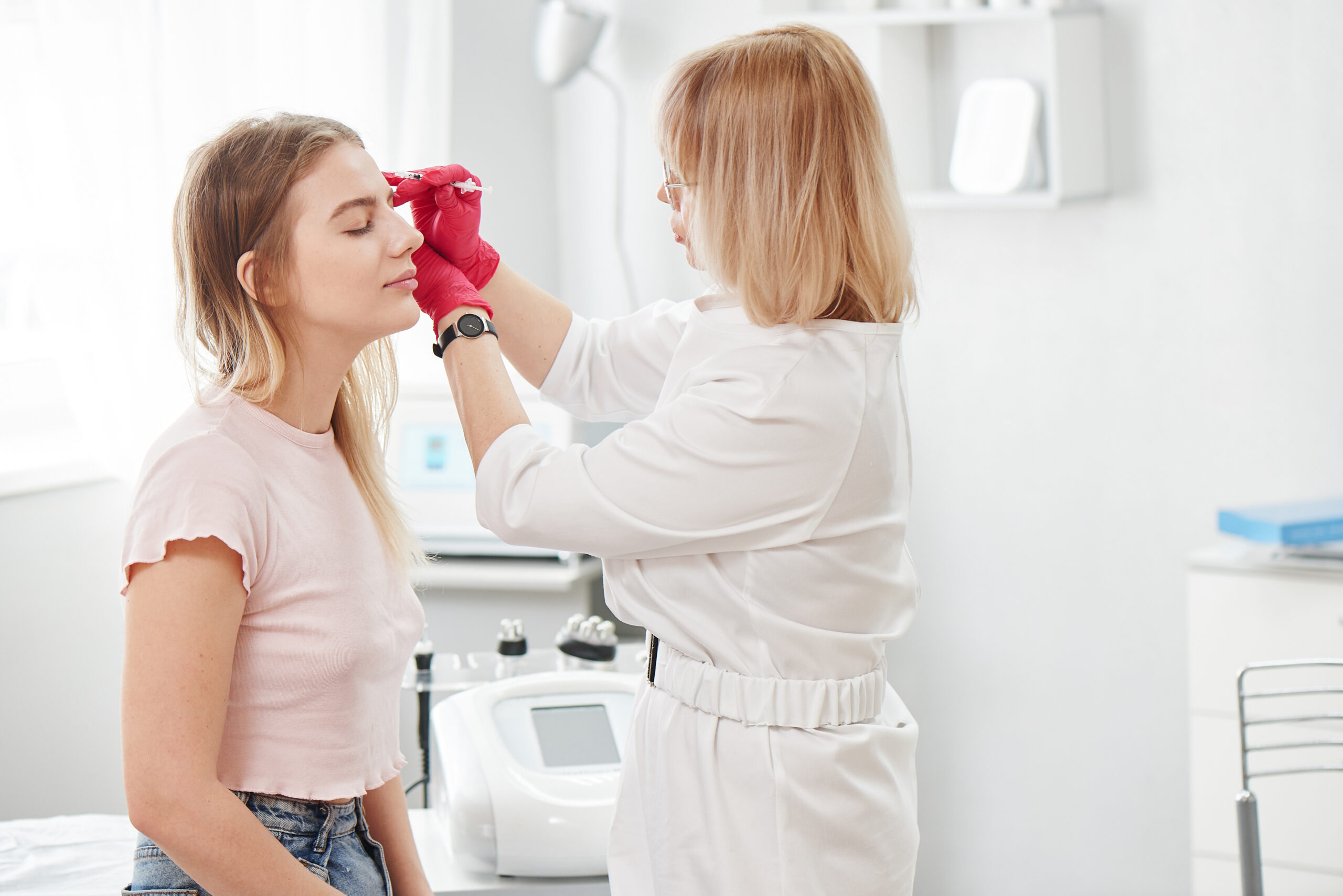 Cosmetologist doctor makes markings on the face of young woman patient, preparing for procedure of botulinum therapy for wrinkles in white beauty parlor
