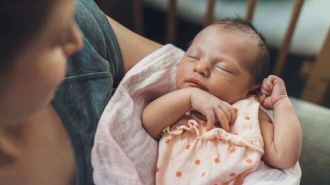 Newborn baby sleeping in safety while mother is holding and smiling at her