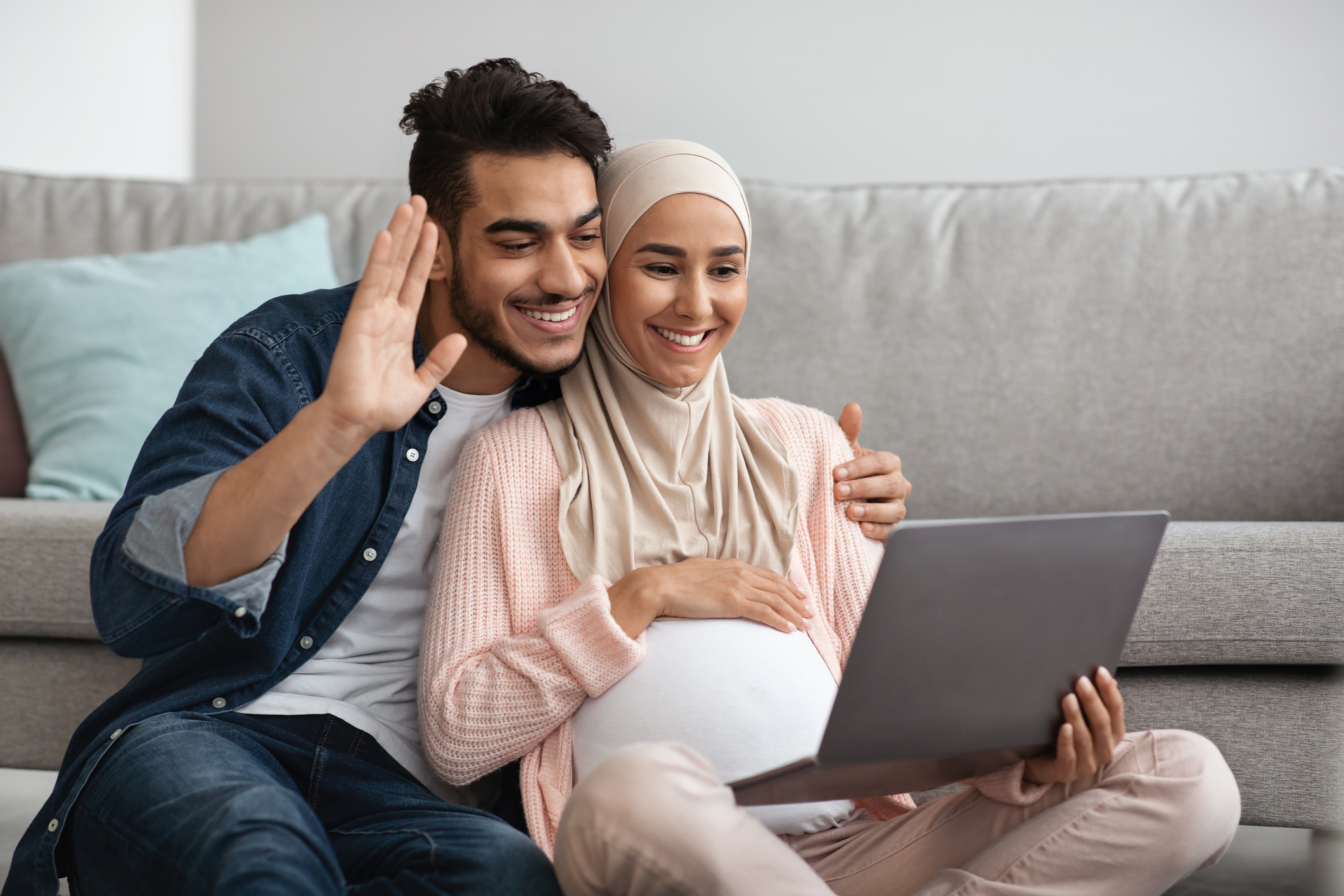 Happy Pregnant Muslim Couple Making Video Call With Laptop At Home