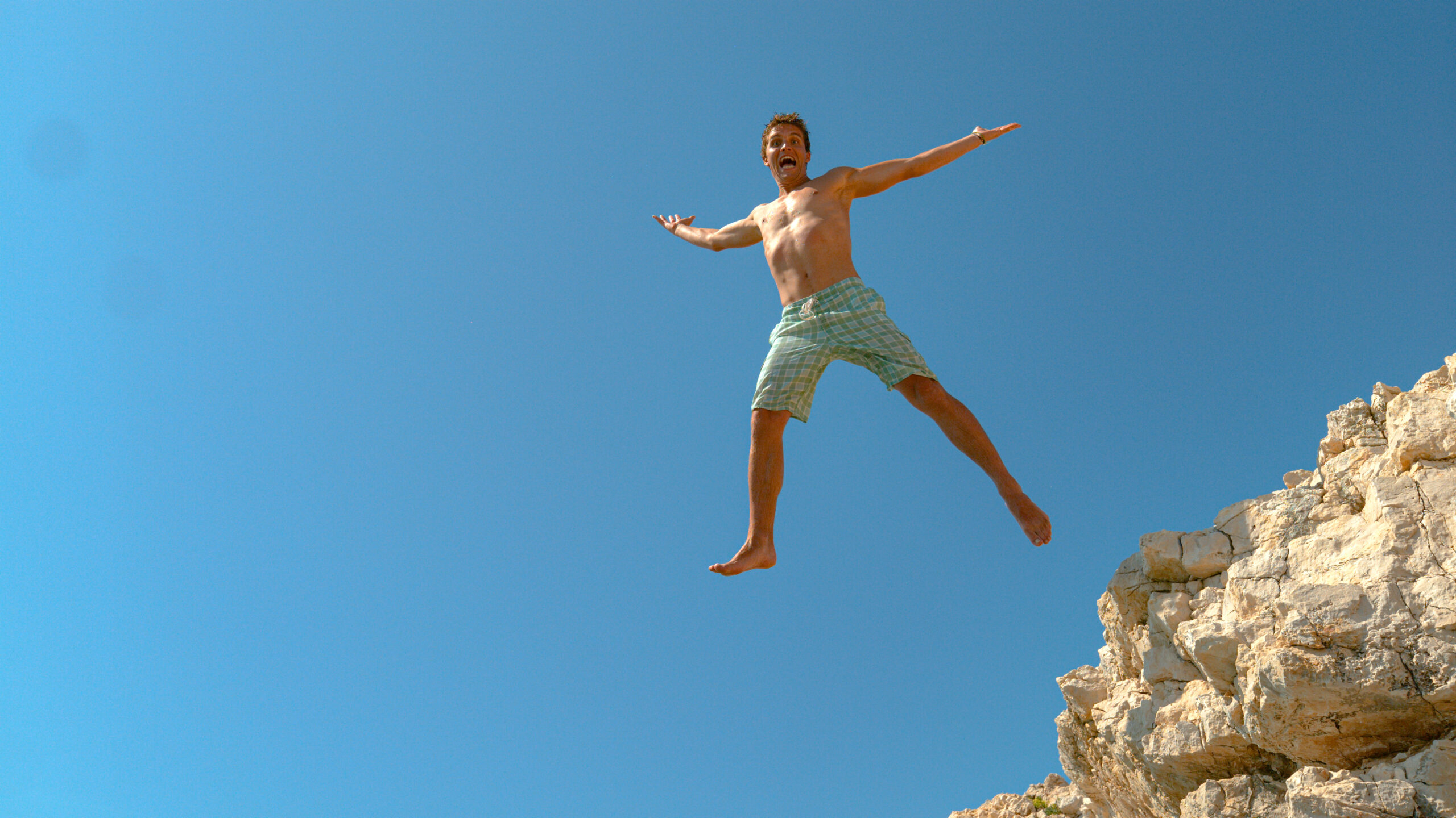 Excited male tourist jumps off edge of a cliff and outstretches arms and legs