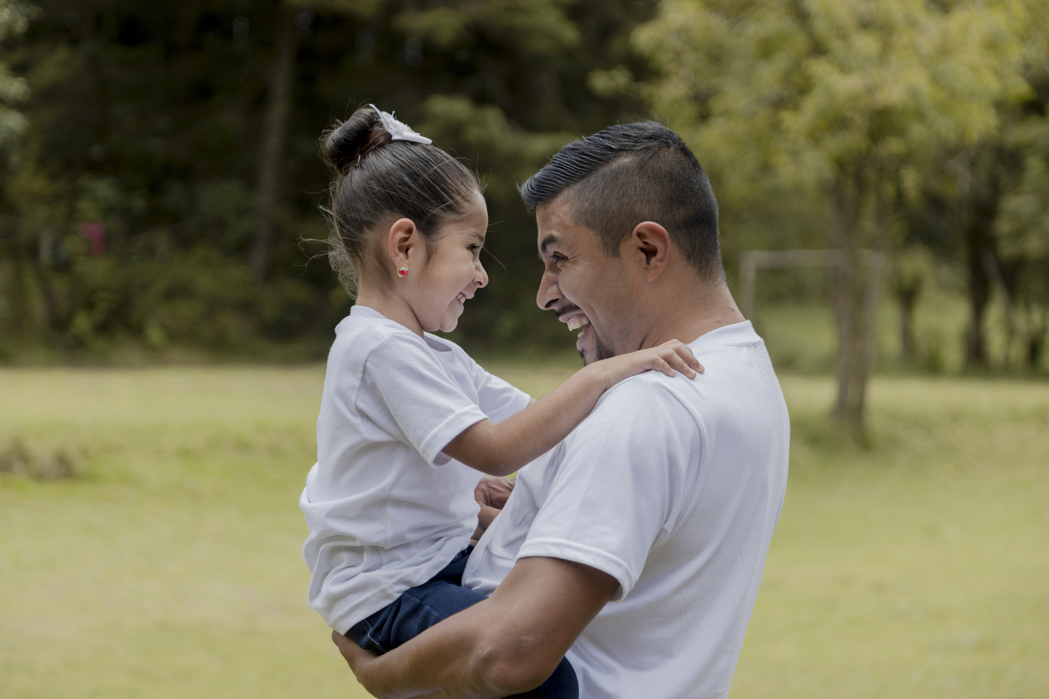 Hispanic dad hugging his little daughter in the park - father and daughter outdoors smiling face to face