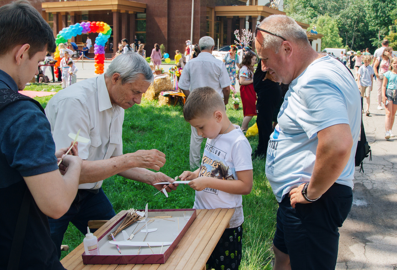 Man volunteer teaching boys to make toy cardboard planes