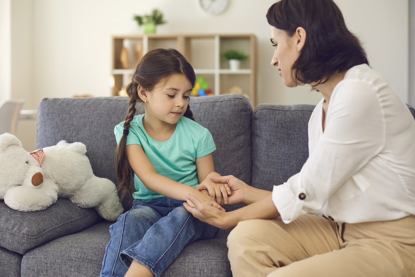Mother sitting with daughter, holding her hands, talking to her and teaching her something