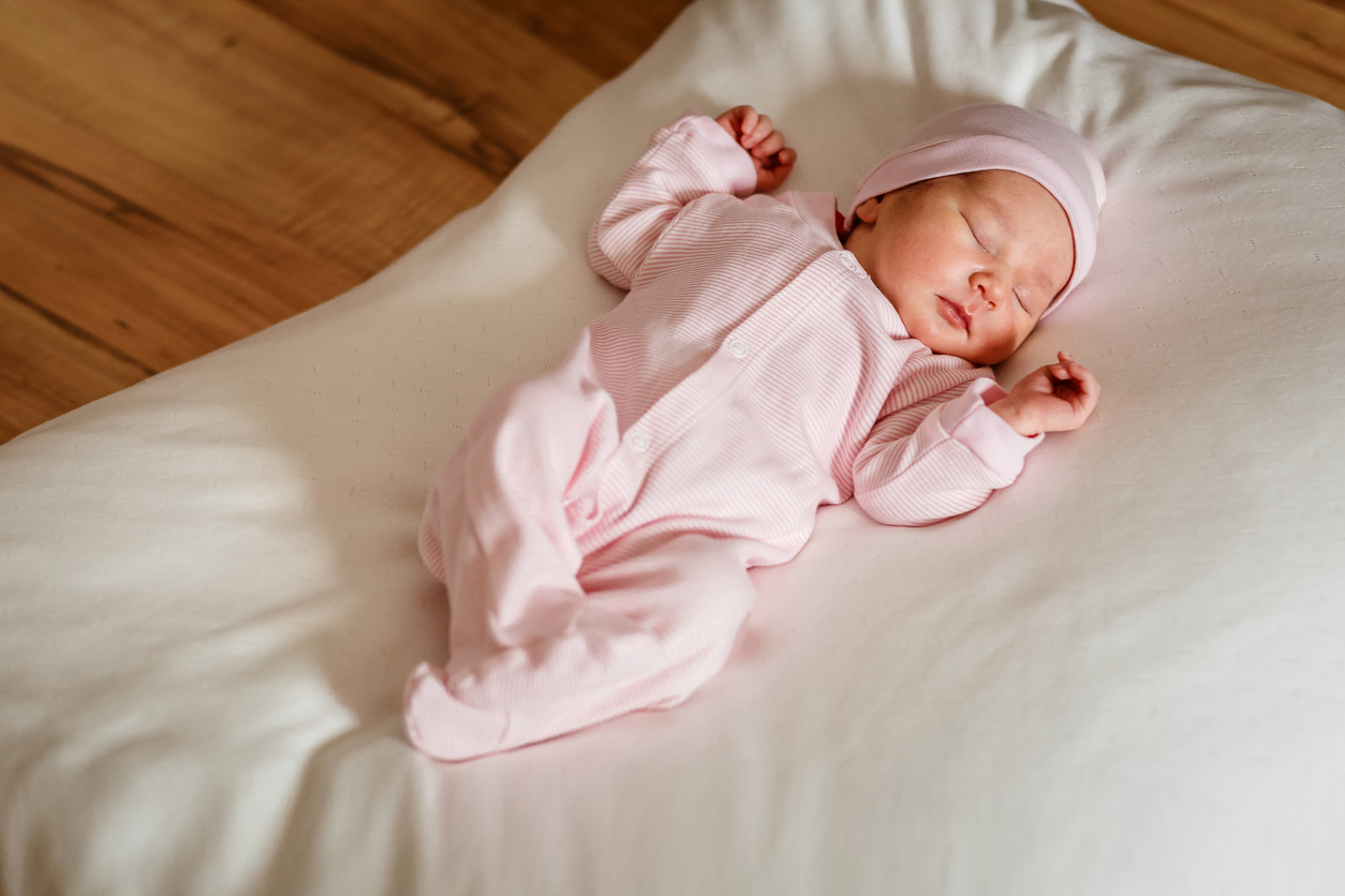 Cute little newborn baby girl of one week sleeps sweetly on white blanket in natural light