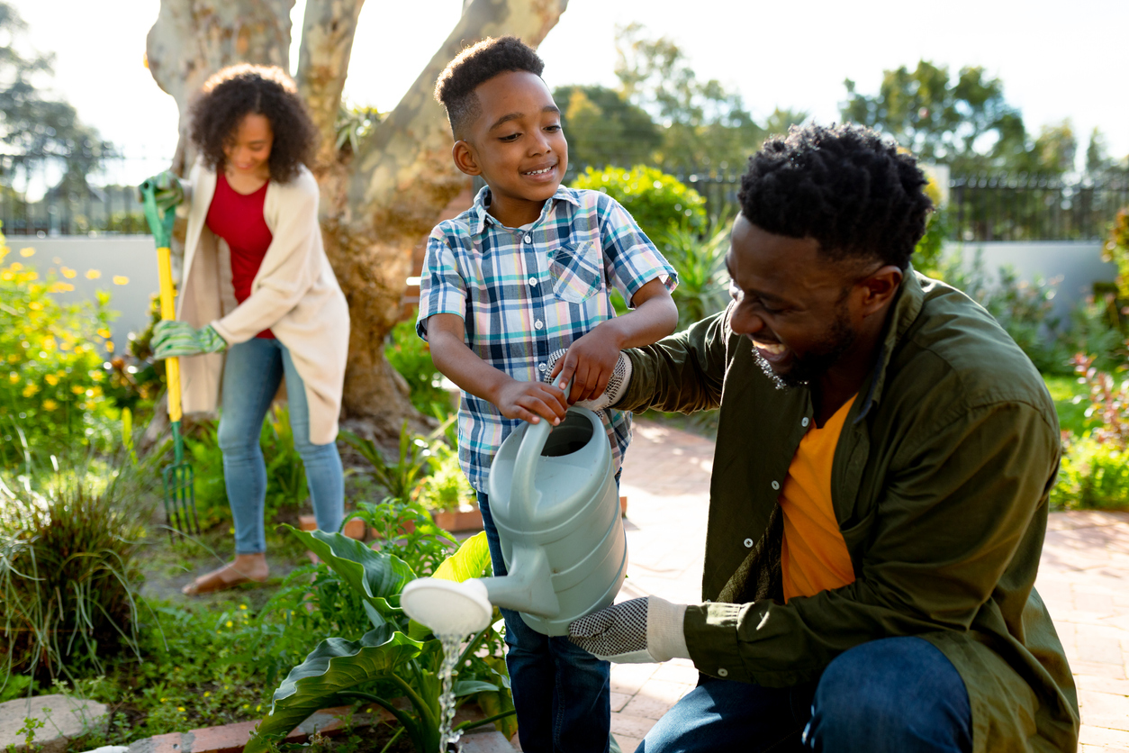 Happy african american father and son watering plants together