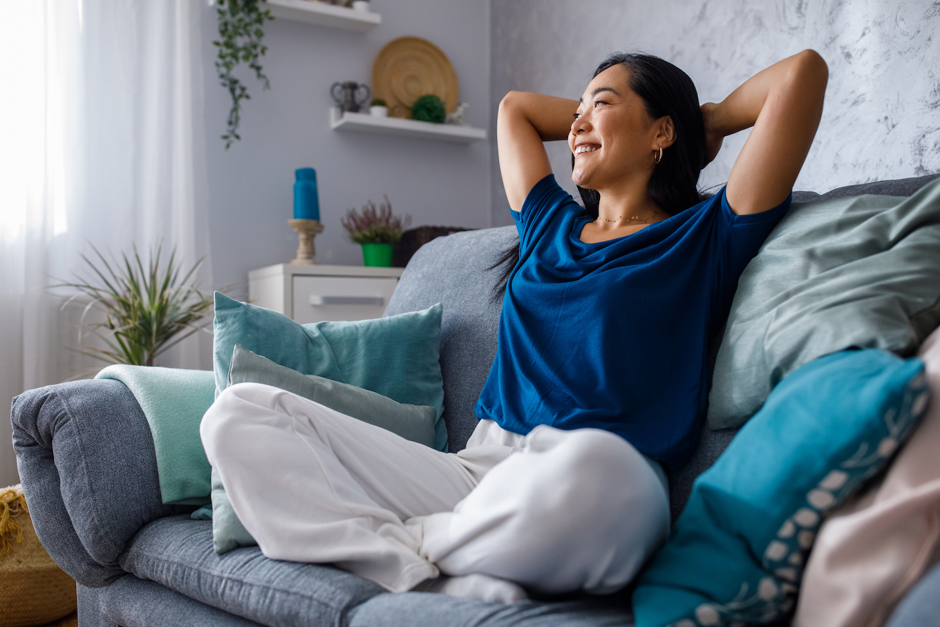 Copy space shot of young woman lounging on sofa with hands behind head and daydreaming