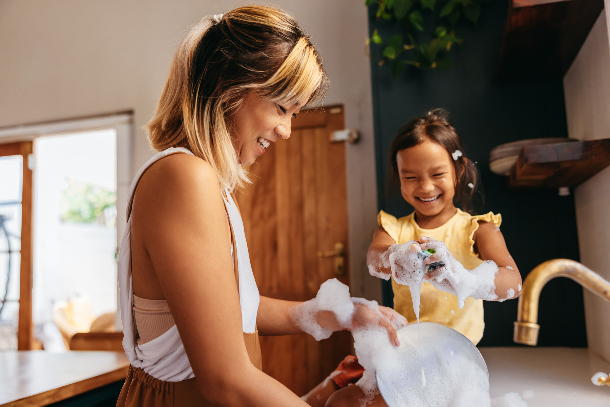 Happy mother and daughter washing dishes in the kitchen