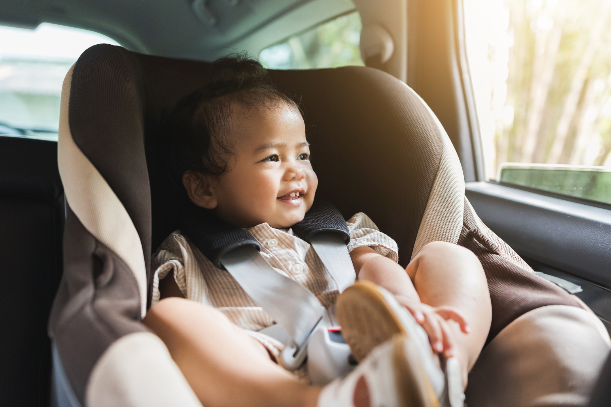 Asian Baby Toddler girl sitting in car seat and looking through window. Infant baby with safety belt in vehicle. Safety car. Family travel concept
