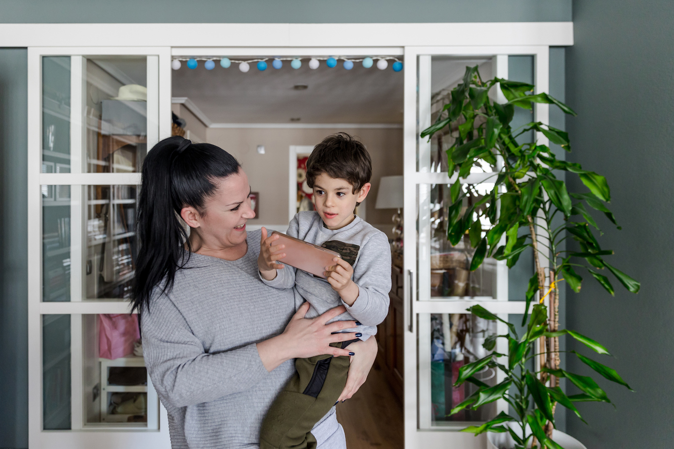 Disabled boy with autism and a lost look, in the arms of his smiling mother while he entertains himself with a mobile phone