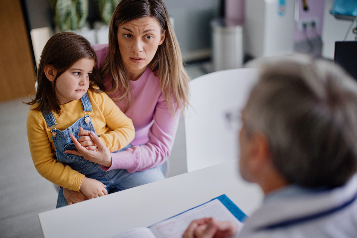 Pediatrician talking to mother and little girl in exam room